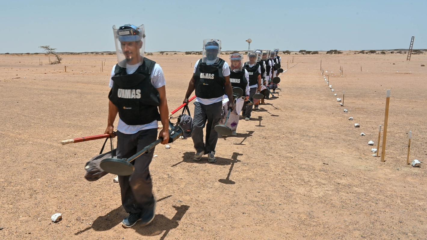 A line of UN de-miners in safety equipment walk through the desert